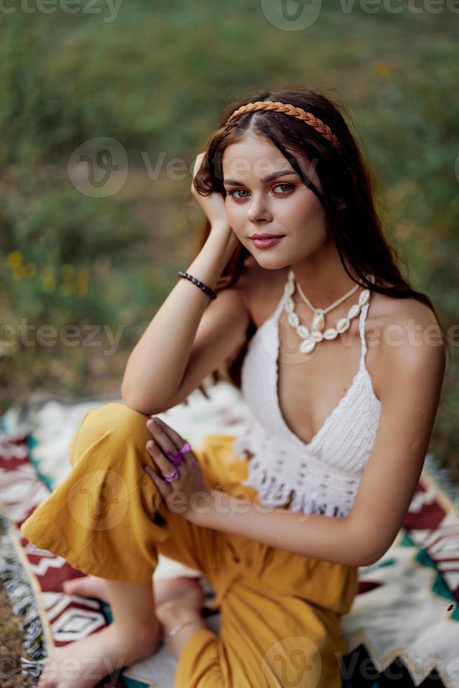 Jeune magnifique hippie femme séance sur le sol dans la nature dans le tomber dans éco Vêtements dans le le coucher du soleil lumière, une mode de vie de Voyage et harmonie avec le monde photo