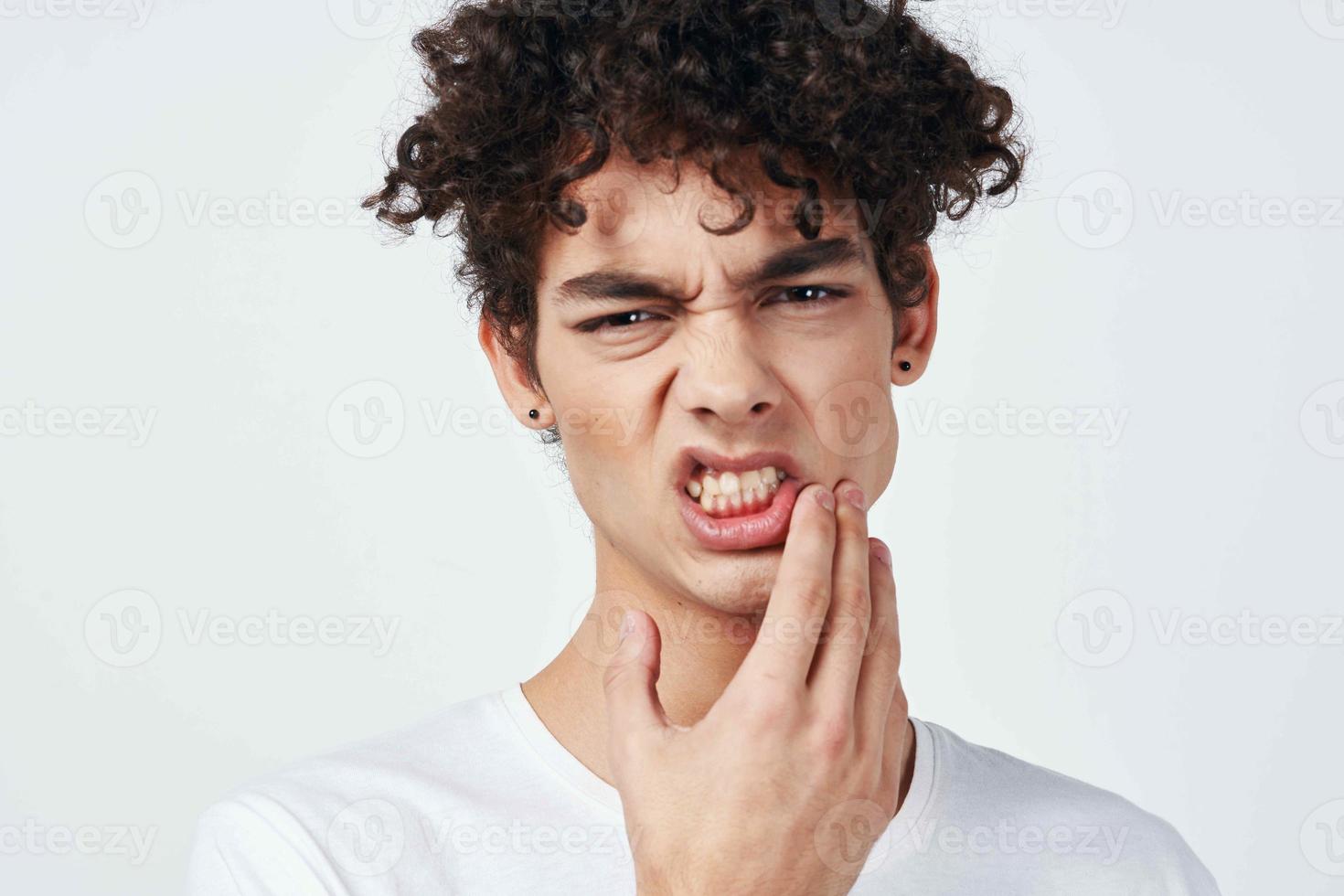 gars dans blanc T-shirt avec frisé cheveux douleur dans le les dents santé problèmes photo