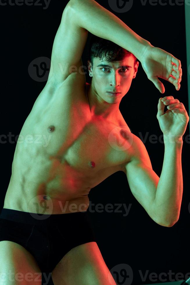 Masculin athlète sur une foncé Contexte posant et montrant muscles sur le abdomen photo