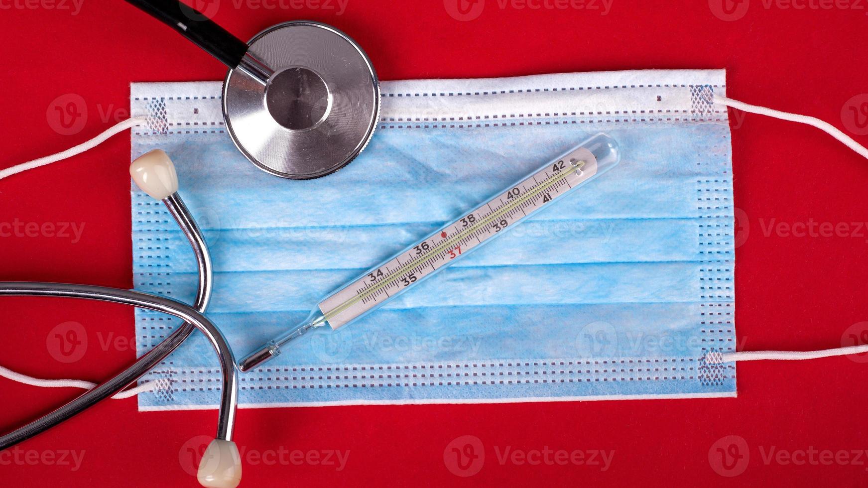 stéthoscope, thermomètre et masque médical jetable sur fond rouge photo