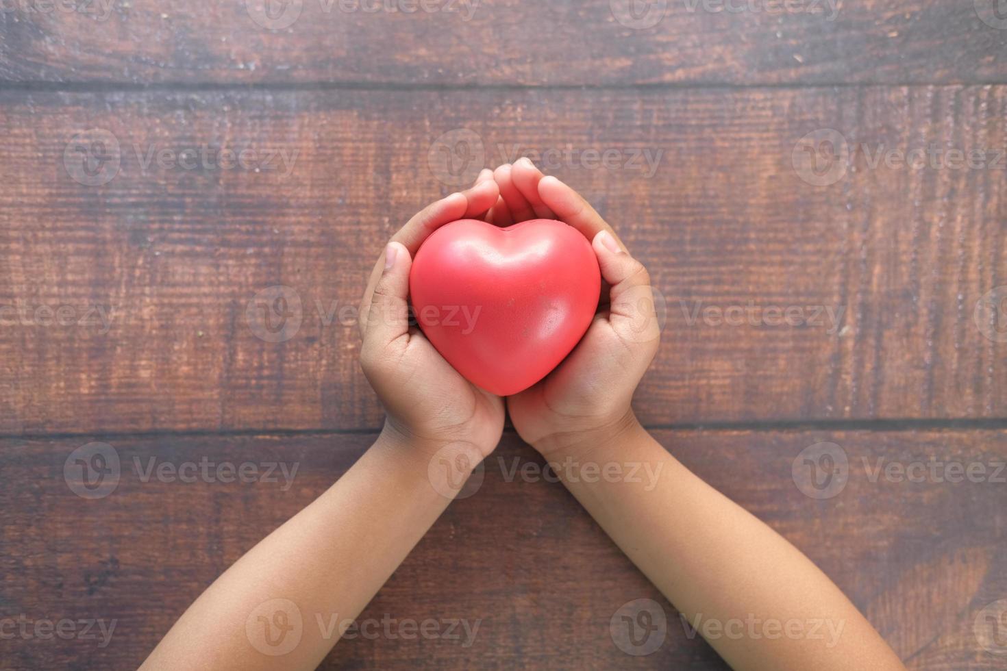 main de l'enfant tenant un coeur rouge sur une table en bois photo