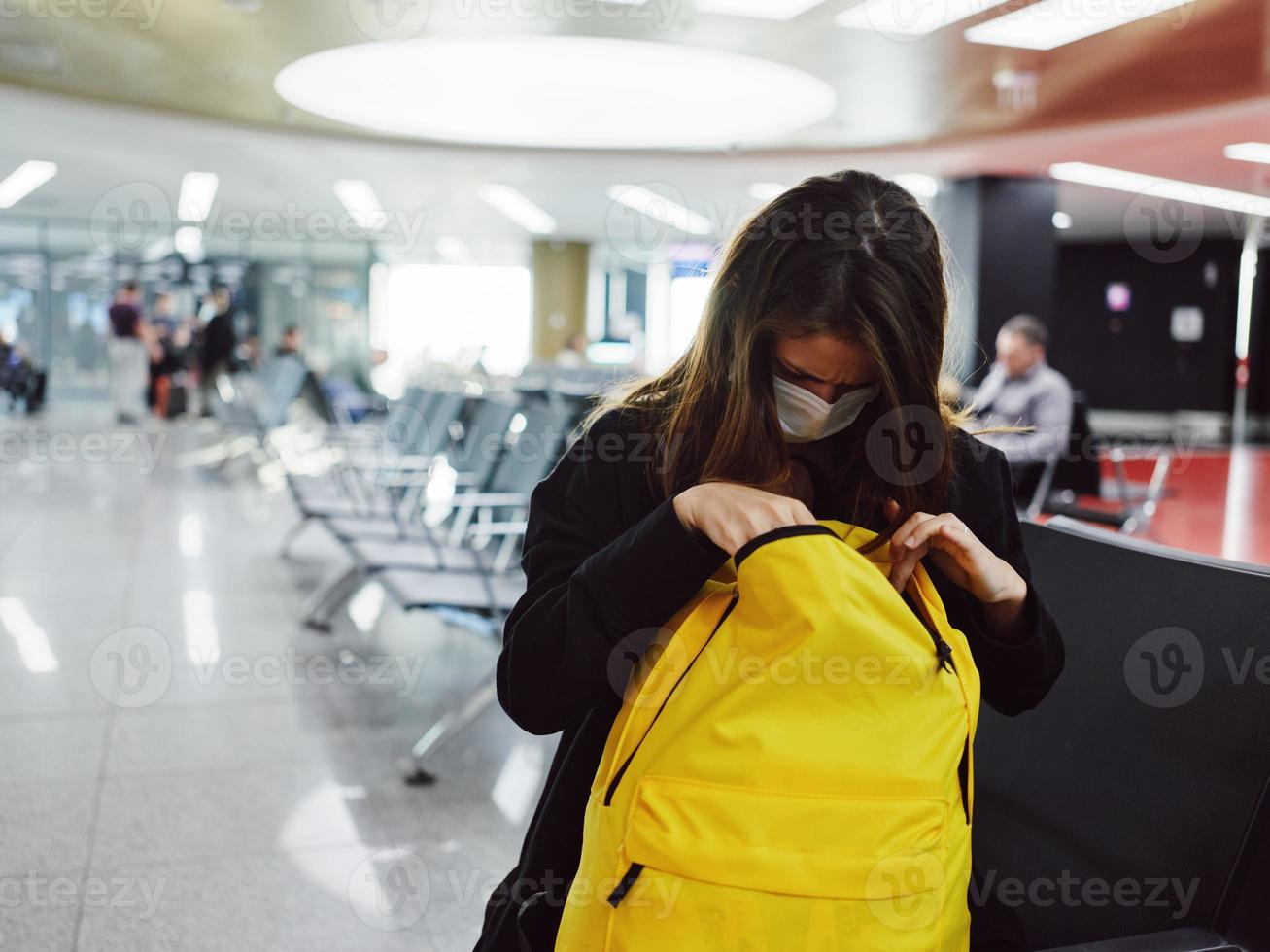 une femme est assis à le aéroport et regards dans une Jaune sac à dos passager photo
