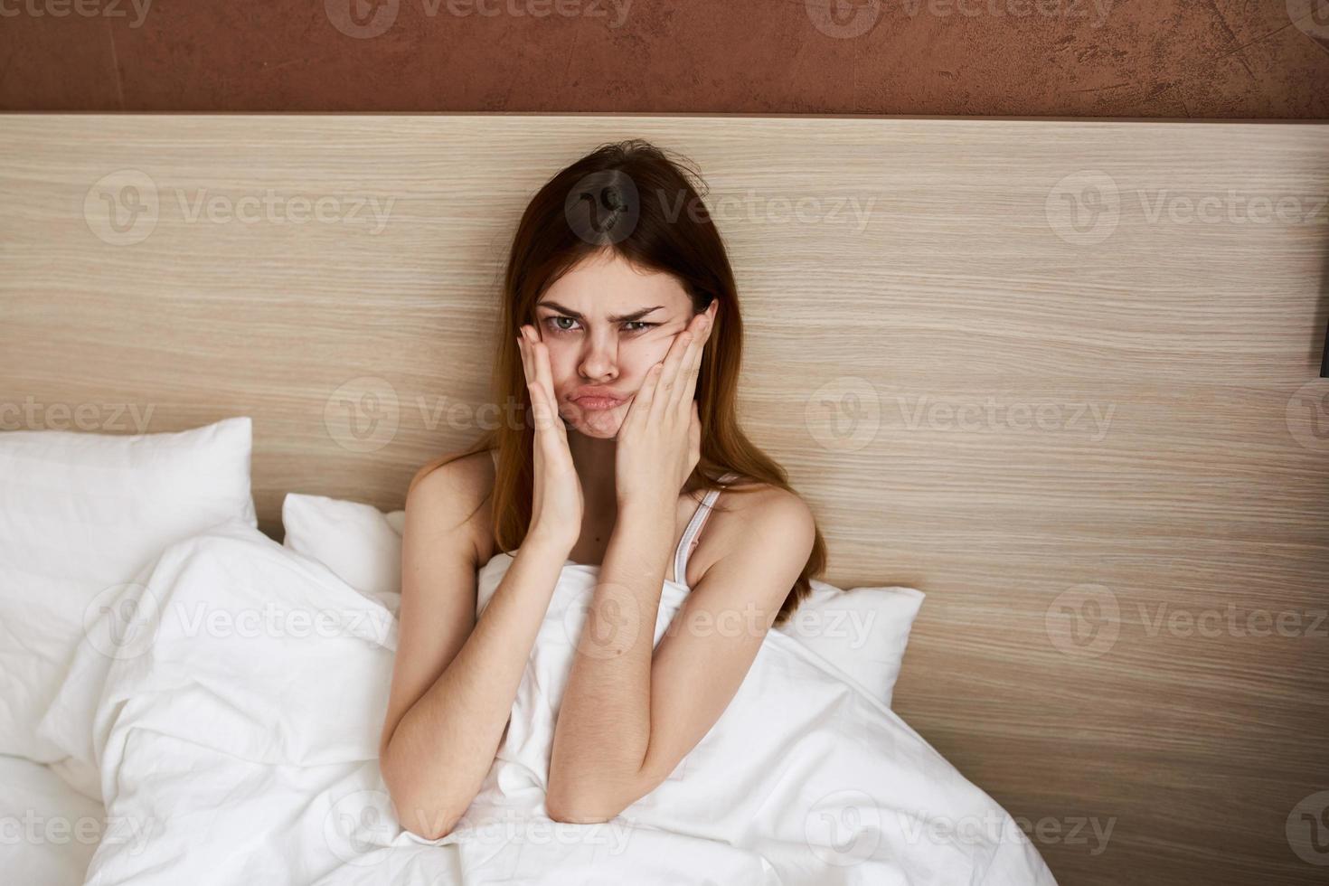 femme réveillé en haut de bonne heure dans le Matin et toucher sa visage avec sa mains en dessous de le couvertures dans lit photo