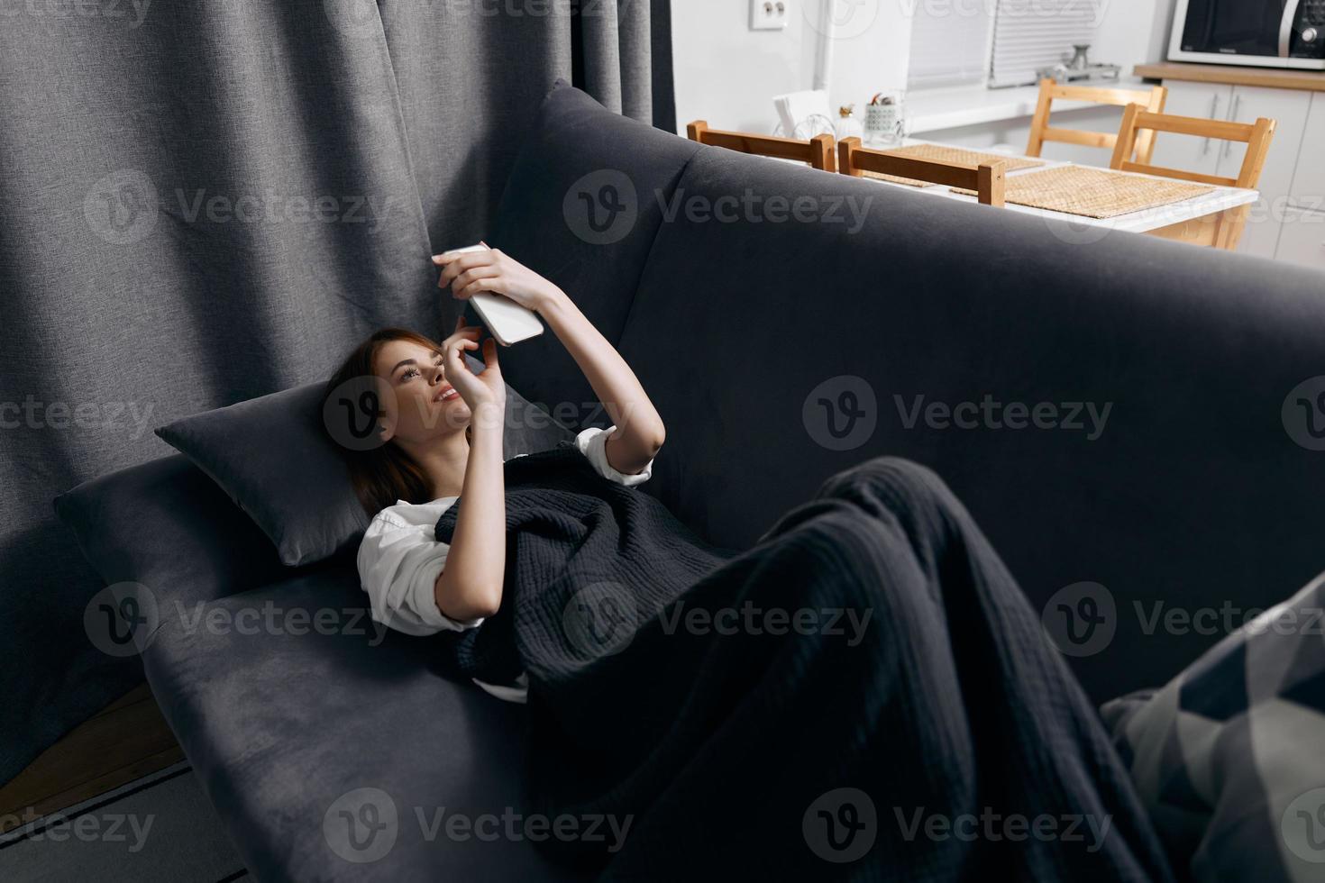 Jeune femme couvert avec une couverture mensonges sur le canapé avec une mobile téléphone dans sa main Haut vue photo