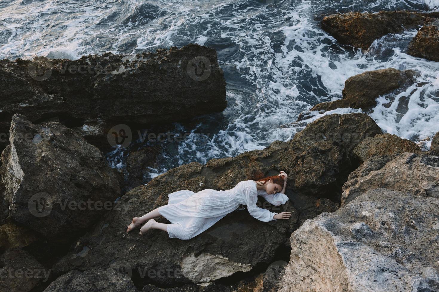 pieds nus femme dans longue blanc robe humide cheveux mensonge sur une rocheux falaise vacances concept photo