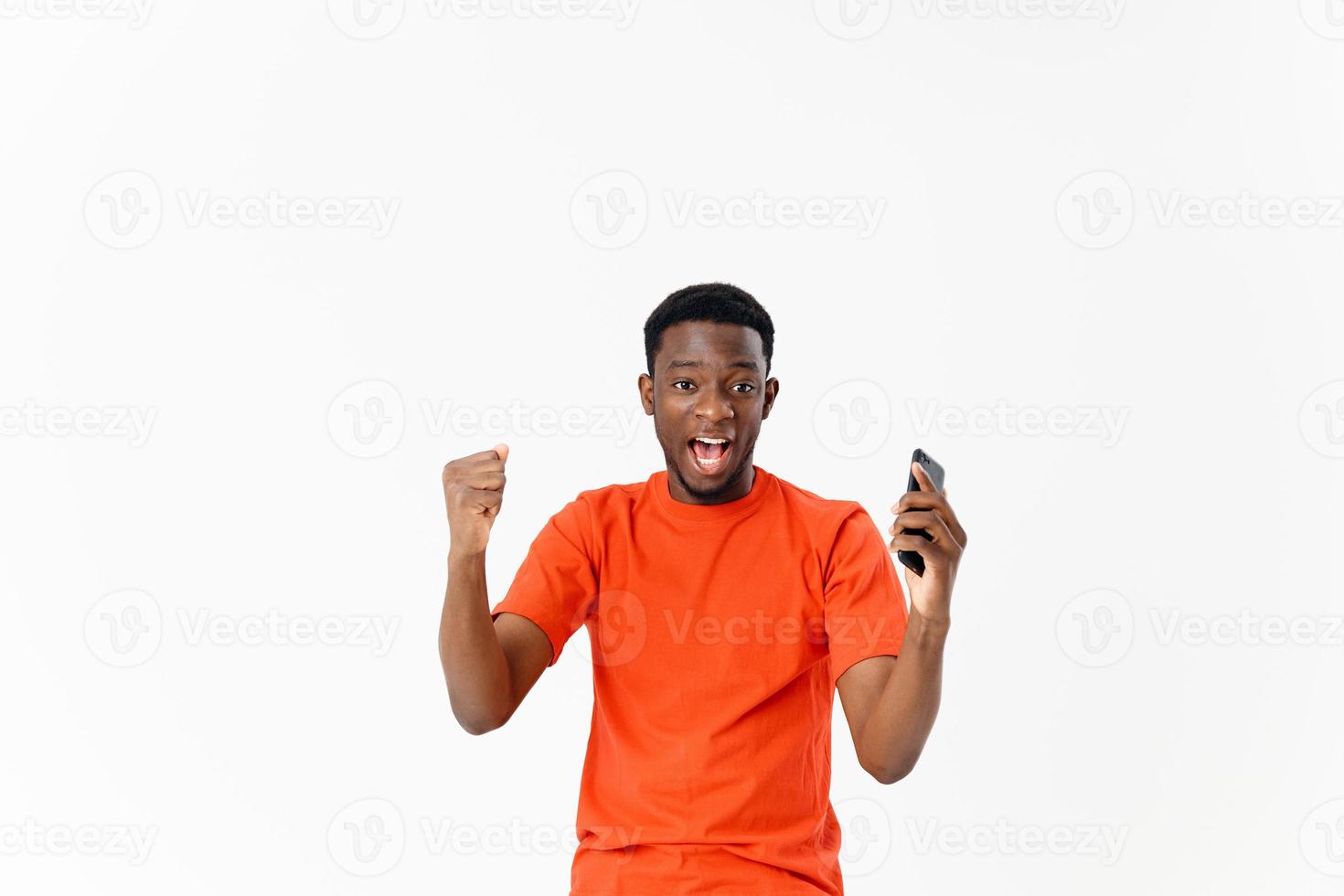 émotif homme dans un Orange T-shirt avec une téléphone dans le sien mains joie studio photo