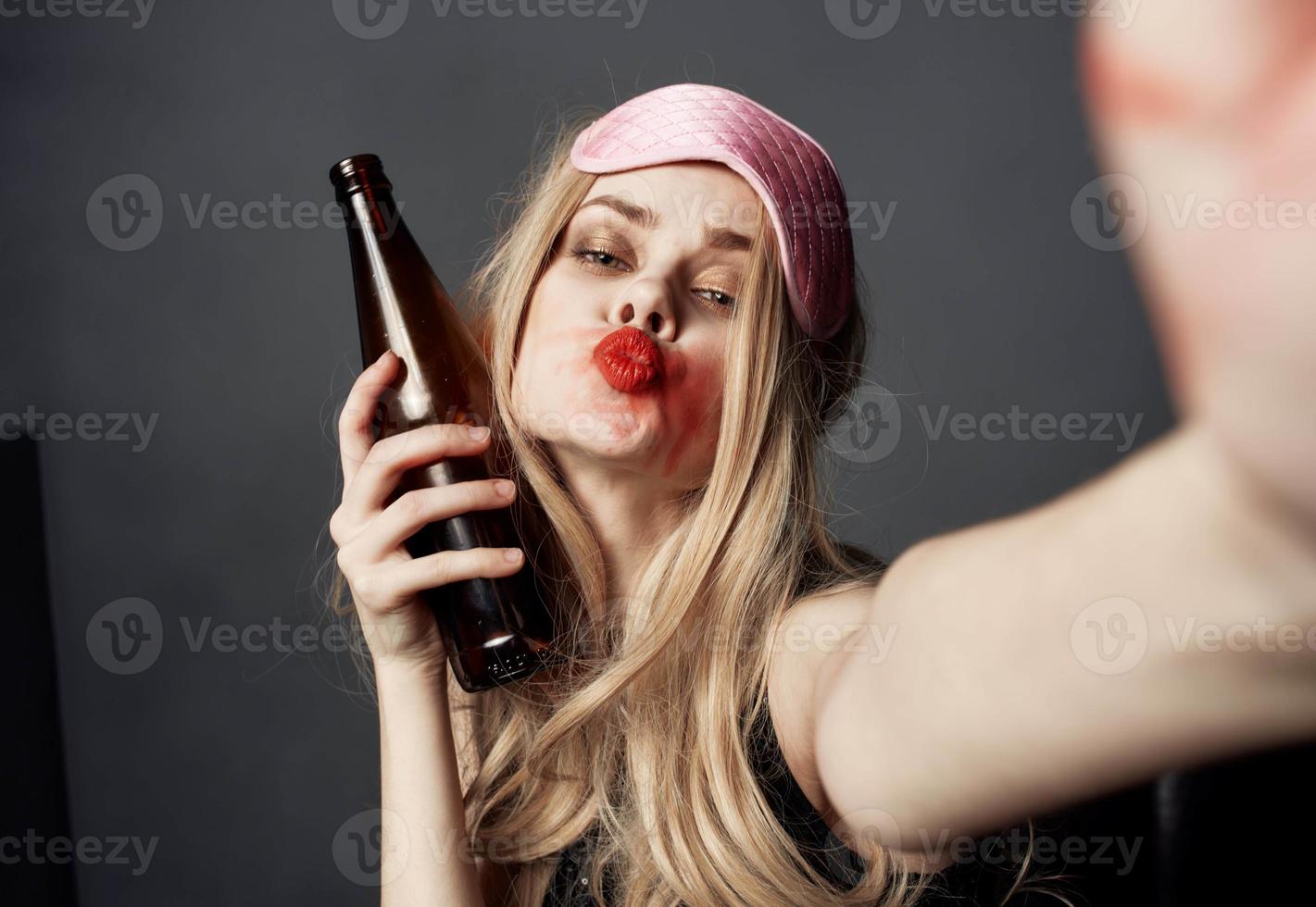 ivre femme avec une bouteille de Bière sur une gris Contexte gestes avec sa mains et brillant maquillage photo