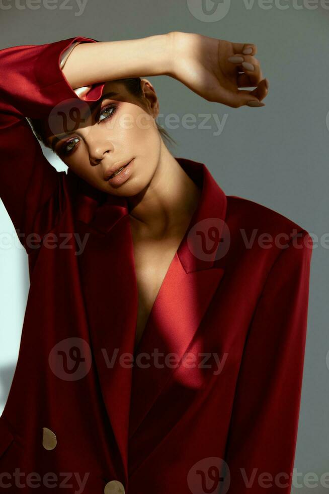 jolie femme avec brillant maquillage détient sa main au dessus sa tête ombres de le lumière rouge veste photo