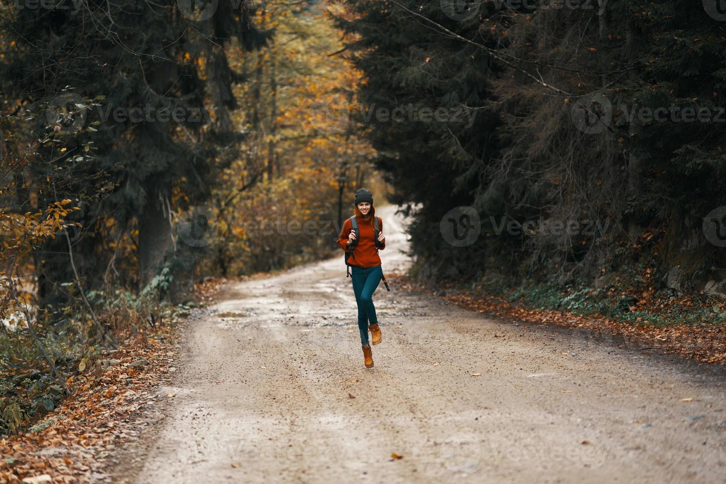 content Voyage avec une sac à dos dans une chaud chandail, pantalon et bottes des promenades le long de le route dans le l'automne forêt photo