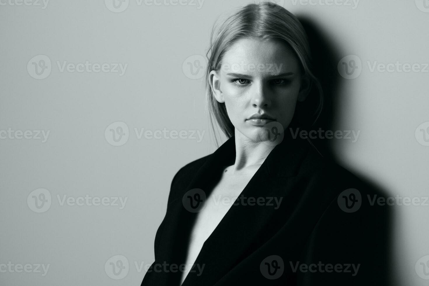 fermer portrait de pensif sérieux blond modèle dans noir veste posant penché sur le studio mur. élégant minimaliste tirer photo