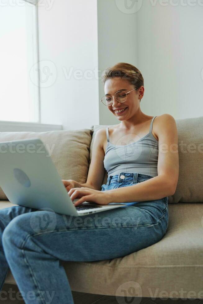 adolescent fille pigiste avec portable séance sur canapé à Accueil souriant dans Accueil vêtements et des lunettes avec court la Coupe de cheveux, mode de vie avec non filtres, gratuit copie espace photo