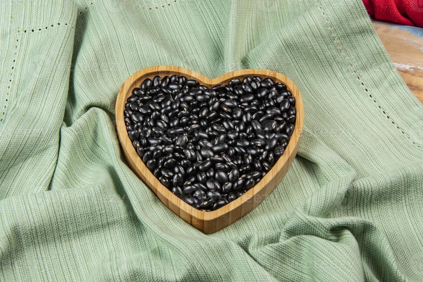 cœur en forme de noir haricot bol sur vert nappe de table photo