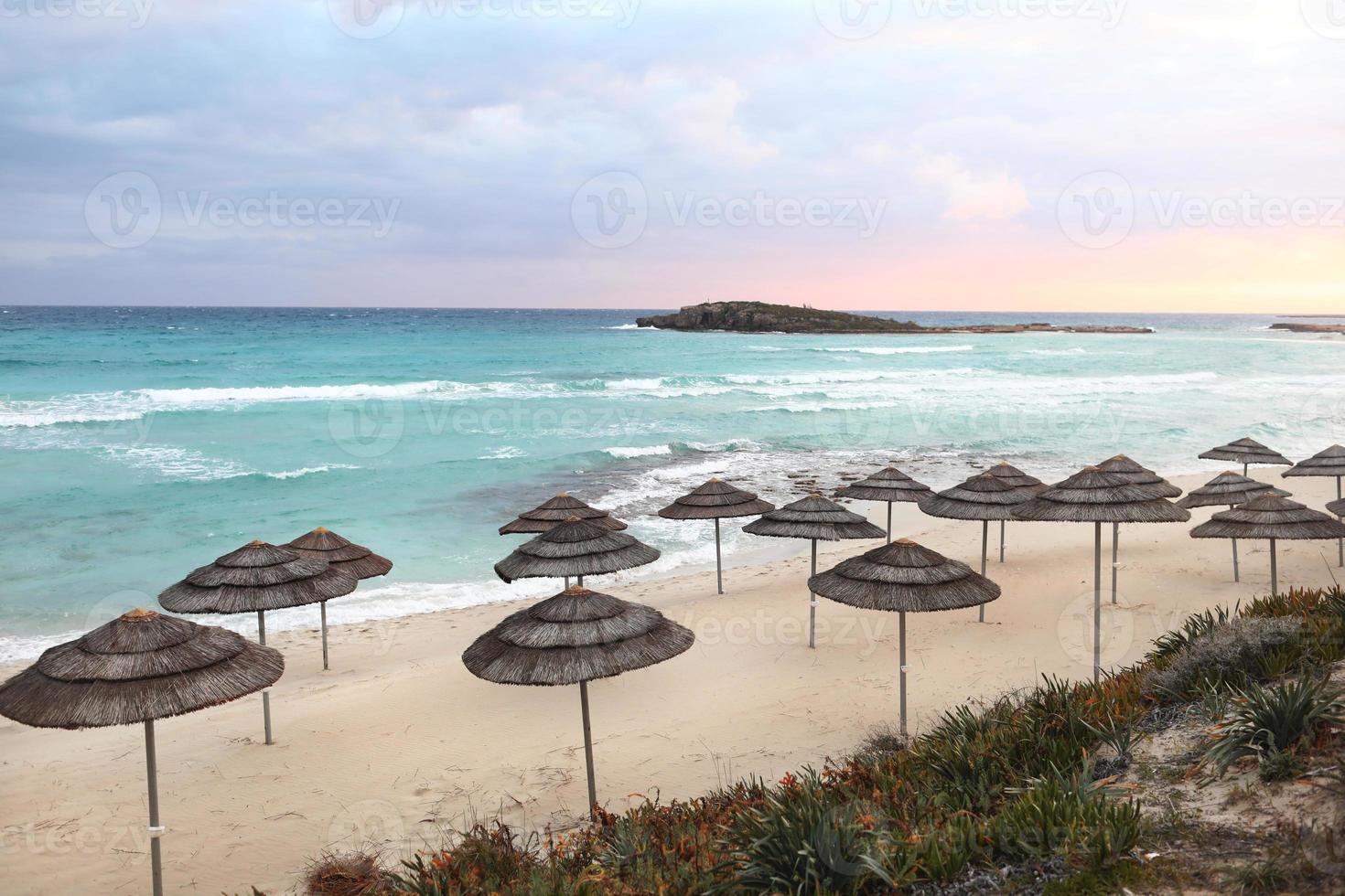 beaux parapluies de paille sur la plage sur la plage vide, eau et ciel bleu vif, plage tropicale paradisiaque, temps de détente, vue imprenable, pas de monde, fond de coucher de soleil. mise au point sélective. photo