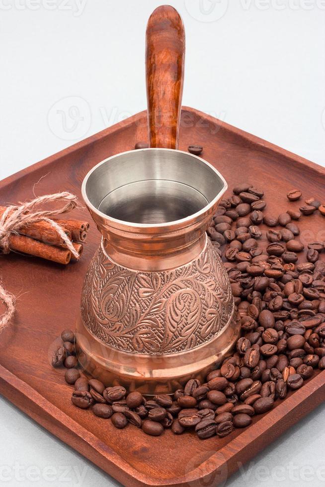 cafetière en cuivre ou ibrik avec grains de café et bâtons de cannelle. sur une planche de bois. fond blanc photo