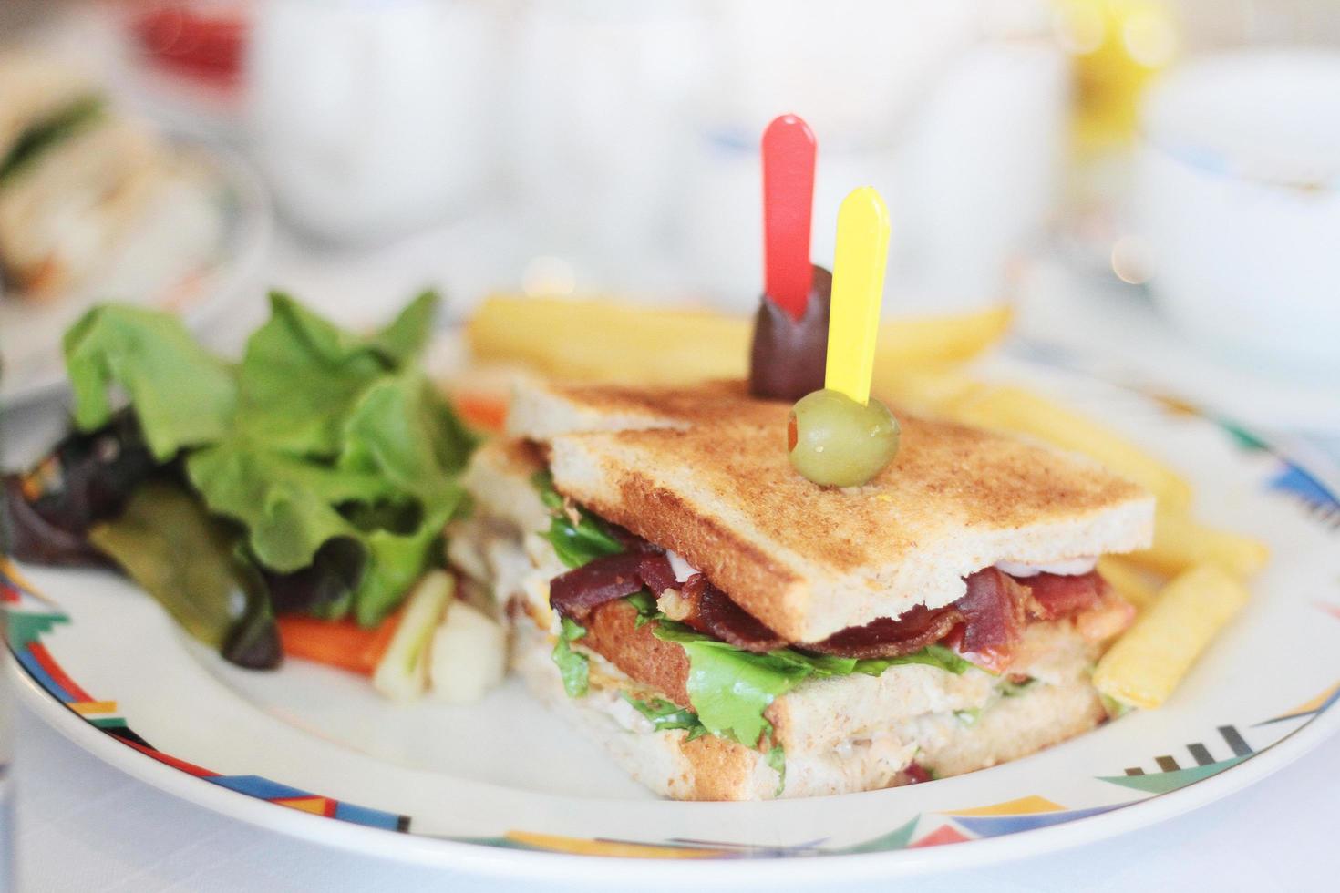 sandwich avec rencontrer, bacon, fromage, français frites, salade, légumes, salade sur une Frais tranché pain sur blanc plaque. photo