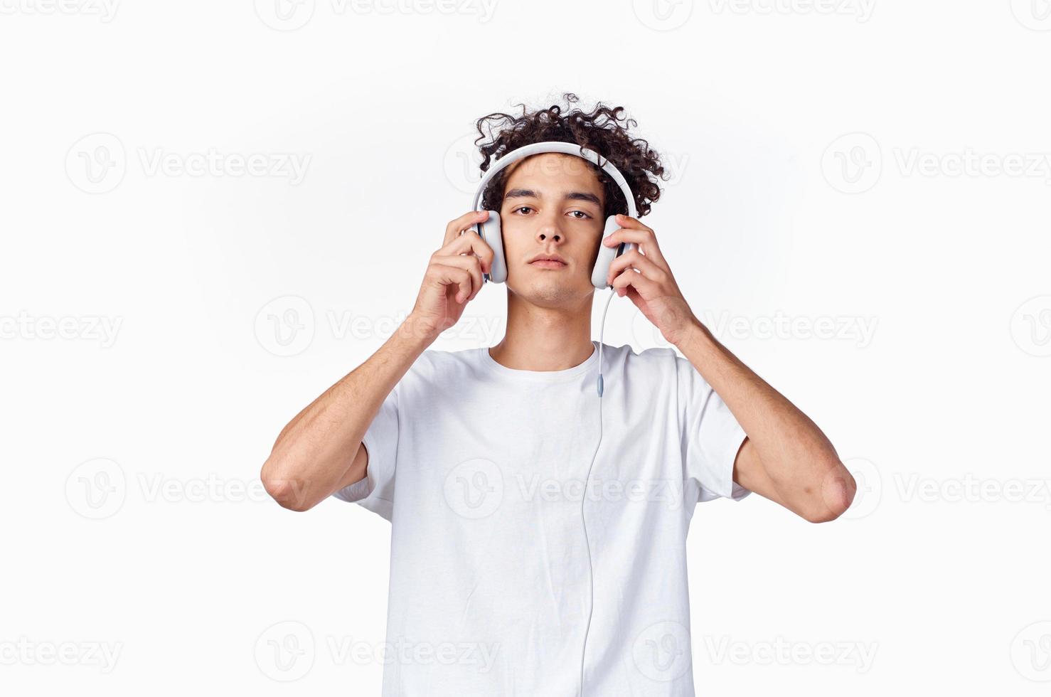 gars avec frisé cheveux et écouteurs blanc T-shirt lumière Contexte fermer tondu photo