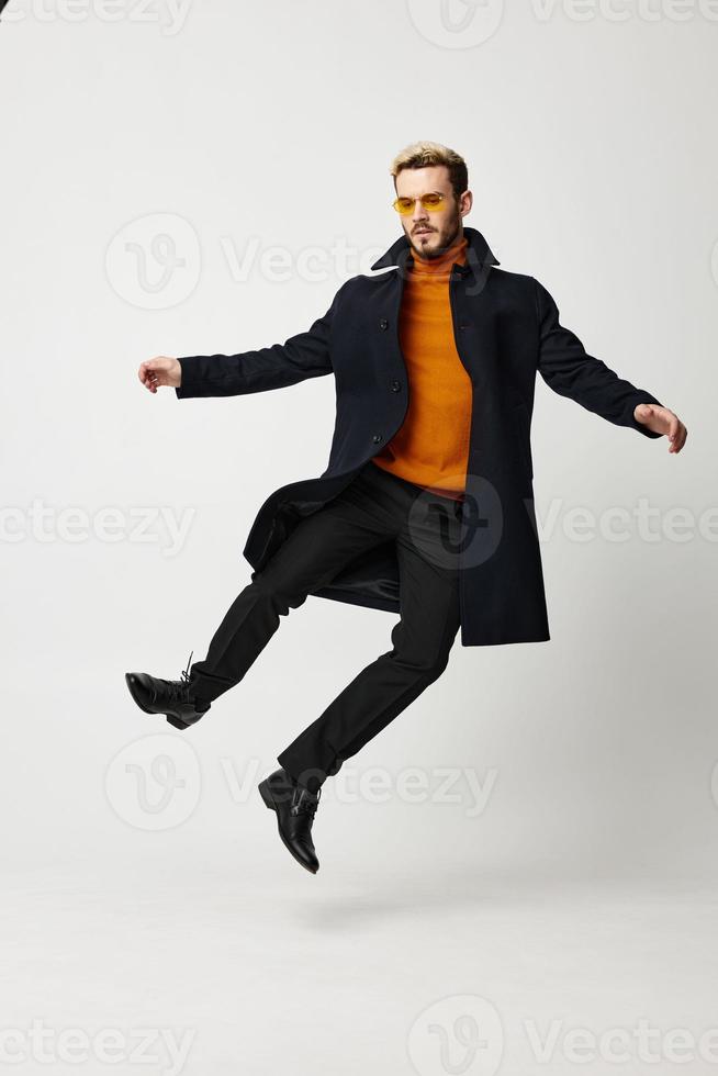 content homme dans une manteau sauté en haut sur une lumière Contexte et à la mode vêtements tendance de le saison photo