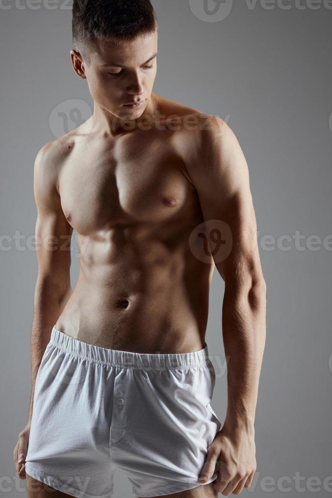 athlète avec une gonflé à bloc torse dans blanc short sur une gris Contexte photo