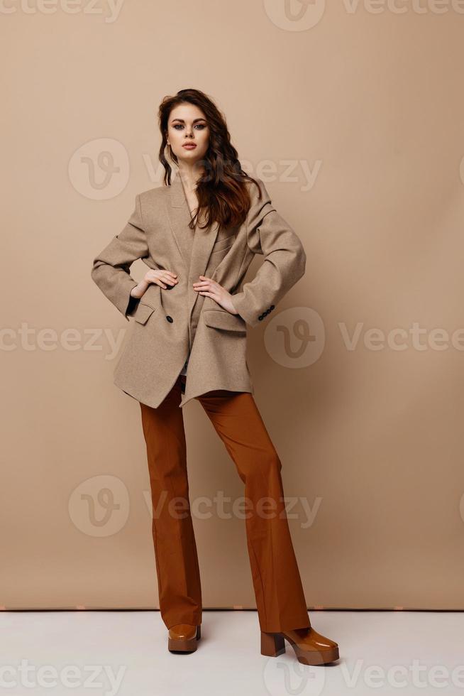 sexy femme dans manteau un pantalon et bottes posant sur une beige Contexte photo