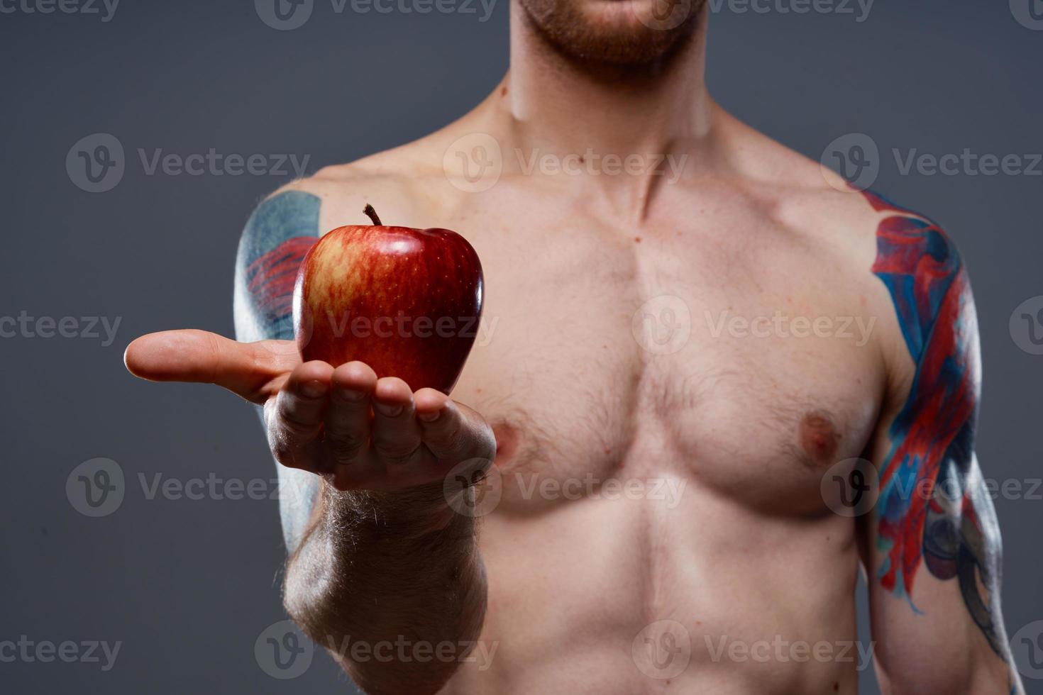 tatoué athlète en portant rouge Pomme sur gris Contexte nu torse tondu vue photo