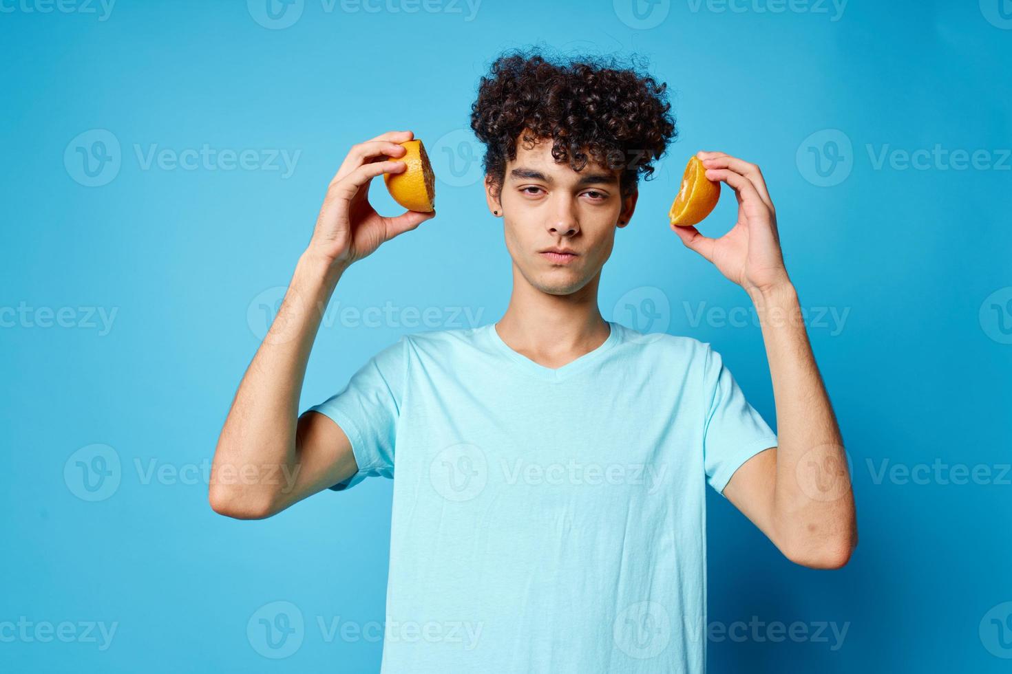 homme avec frisé cheveux des oranges en portant fruit studio bleu Contexte photo