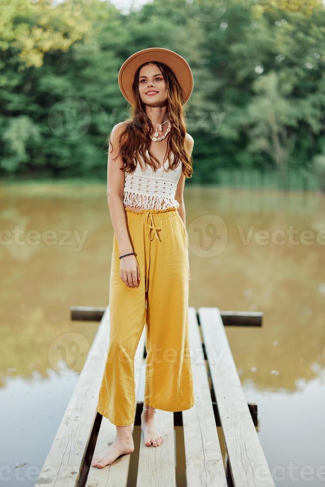 une Jeune femme dans une hippie Regardez et éco Vêtements voyages en plein air par le Lac portant une chapeau et Jaune un pantalon dans le tomber photo