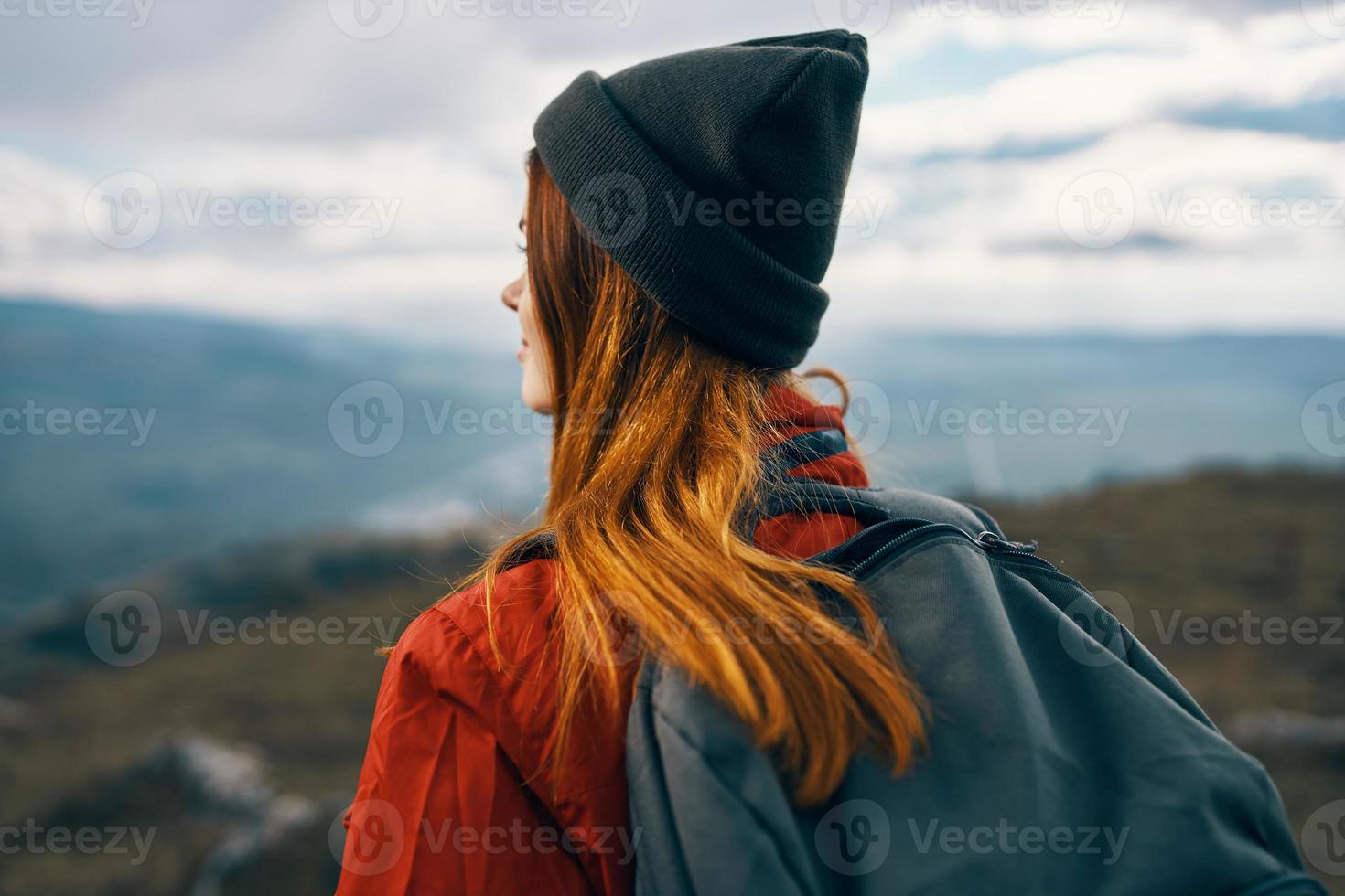 femme dans une veste chapeau et une sac à dos regards à le montagnes dans le distance dans la nature photo