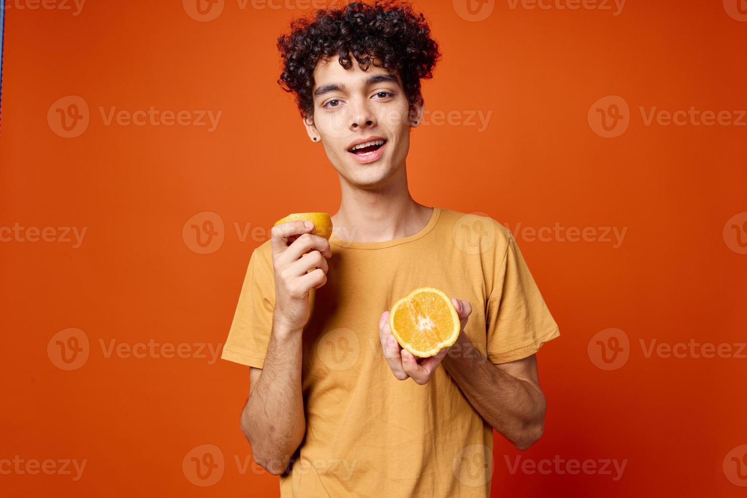 frisé gars dans une Jaune T-shirt des oranges dans le sien mains rouge Contexte photo