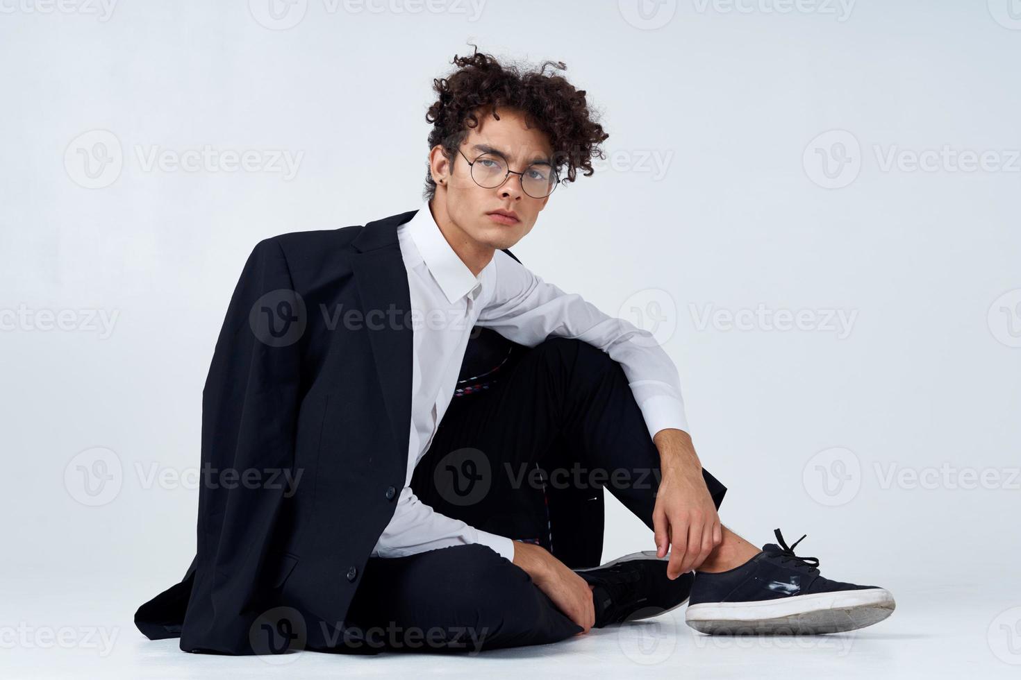 élégant homme avec frisé cheveux dans baskets sur une lumière Contexte une veste sur le épaule un pantalon modèle photo