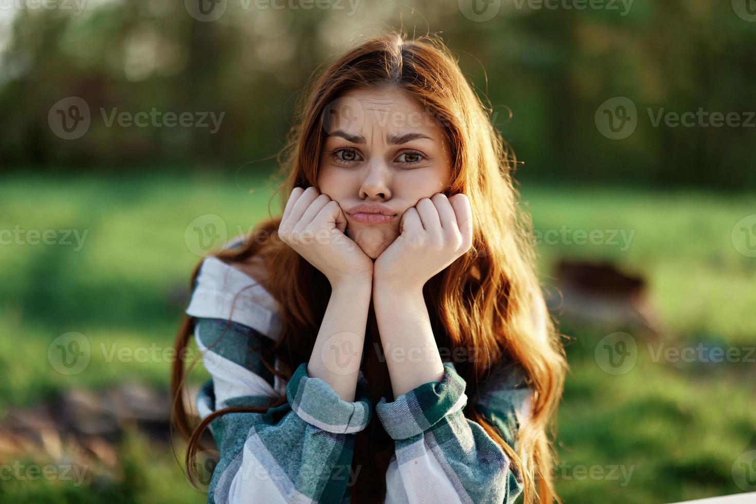 une femme est assis dans la nature dans le parc avec sa mains en dessous de sa tête et regards Malheureusement dans le caméra, faire la moue avec rancœur photo