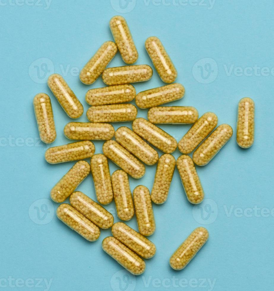 transparent médical capsules avec Jaune granules à l'intérieur sur une bleu arrière-plan, comprimés pour traitement, vitamines photo