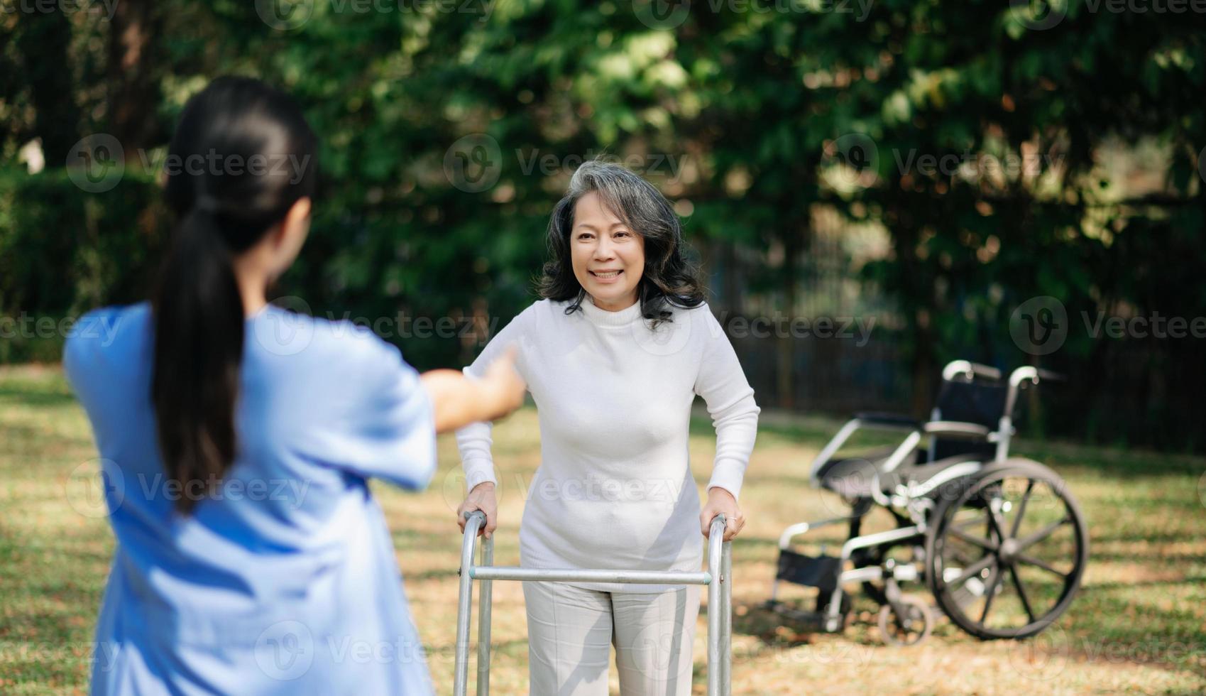 asiatique prudent soignant ou infirmière et le content patient dans une fauteuil roulant sont en marchant dans le jardin à Aidez-moi et encourager et du repos votre esprit avec vert la nature. Aidez-moi soutien toi même à apprendre à marcher. photo