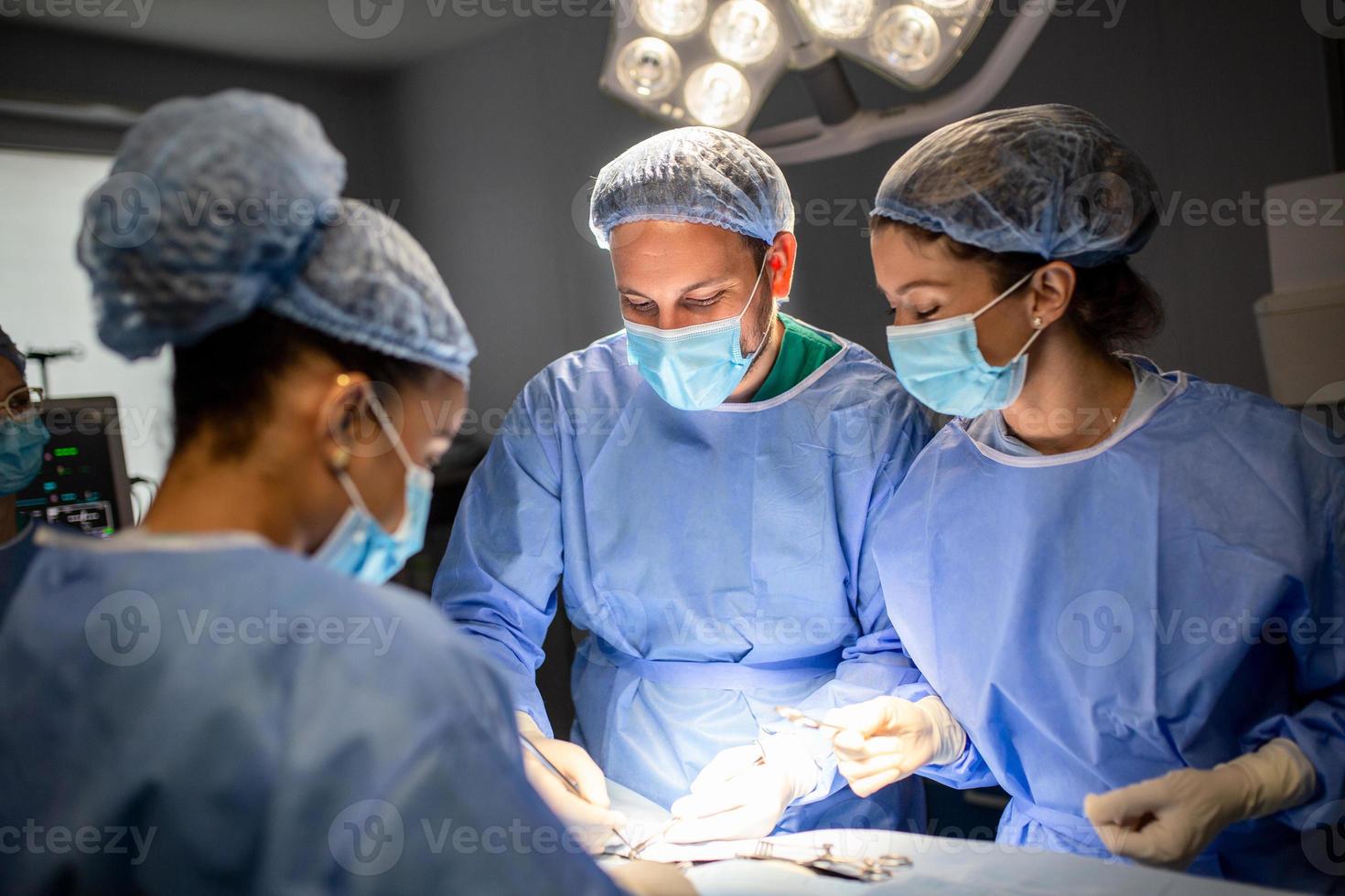groupe de chirurgiens pratiquant la chirurgie dans le bloc opératoire de l'hôpital. équipe médicale effectuant une opération critique. groupe de chirurgiens en salle d'opération avec équipement chirurgical. formation médicale moderne photo
