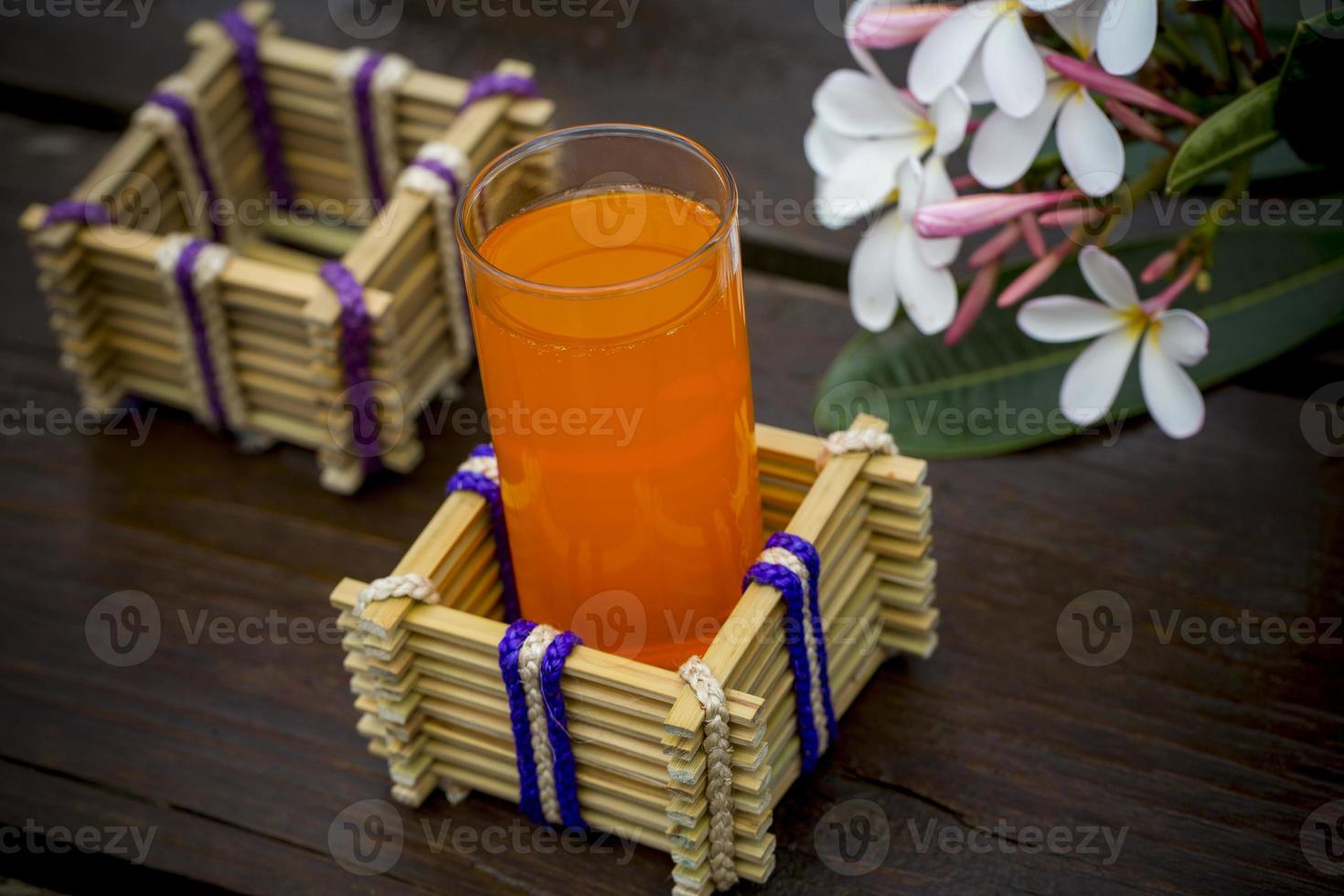 une verre de Orange jus avec l'eau verre titulaire fabriqué de bambou des bâtons et fibre. décoratif en bois table avec magnifique plumeria fleurs. bambou verre titulaire. photo