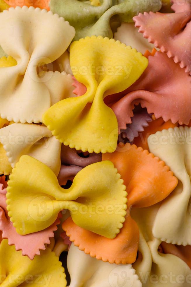 brut farfalle Pâtes dans différent couleurs sur une foncé béton Contexte photo