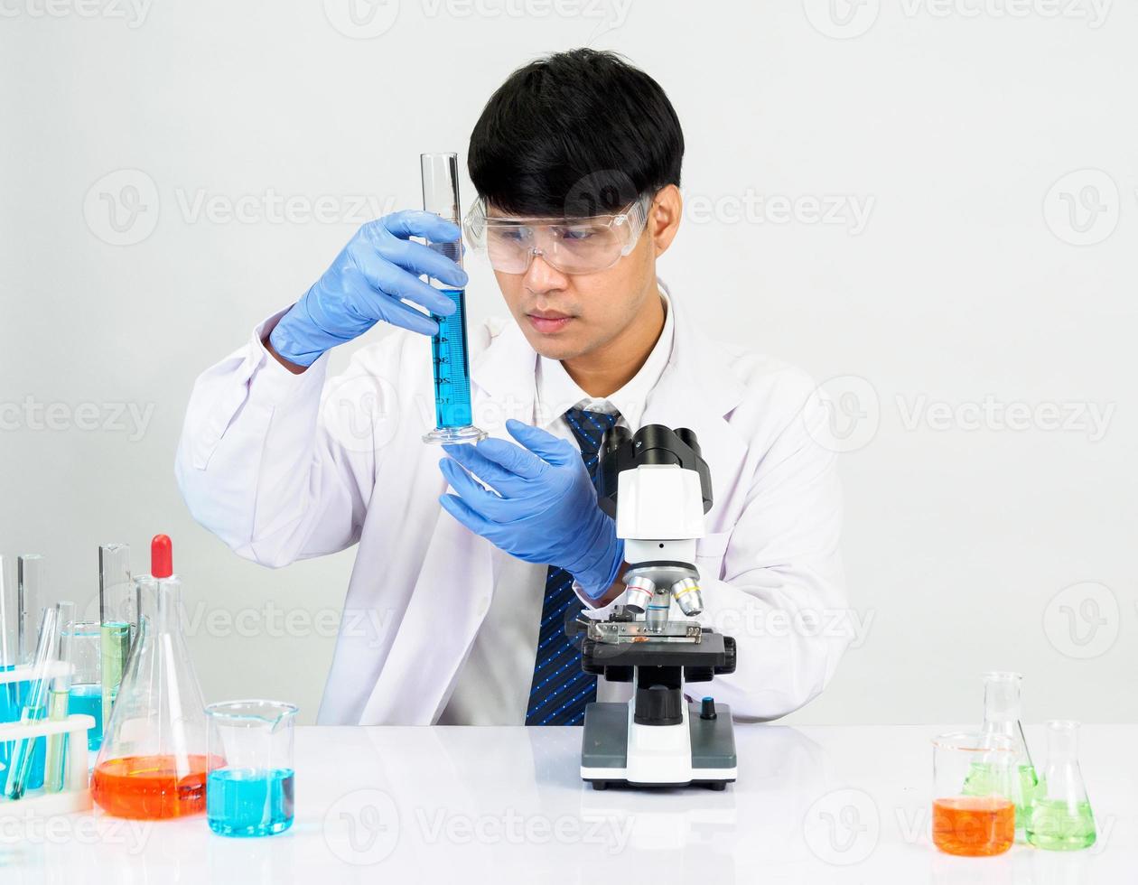 asiatique Masculin étudiant scientifique portant une médecins robe dans le laboratoire à la recherche main à chimiste. causé par mélange réactifs dans scientifique recherche laboratoires avec tester tubes et microscope sur le table photo