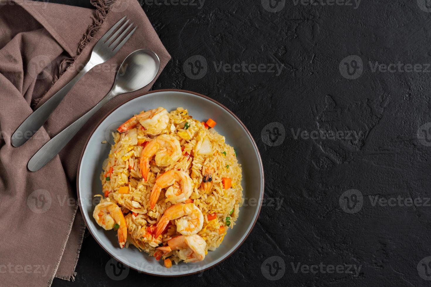 frit riz avec des légumes et mer crevettes, carottes, œufs, et tomates. thaïlandais chinois nourriture est arrangé sur une noir assiette sur une noir Contexte cuisine tableau, Haut voir. photo