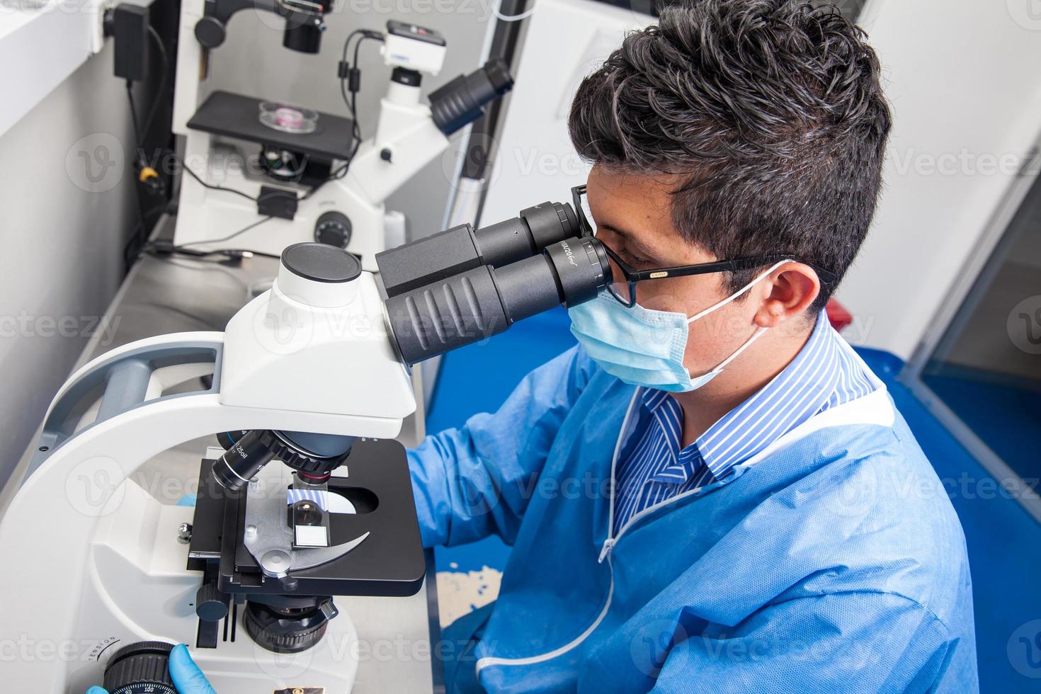Jeune Masculin scientifique à la recherche à diapositives en dessous de le microscope photo
