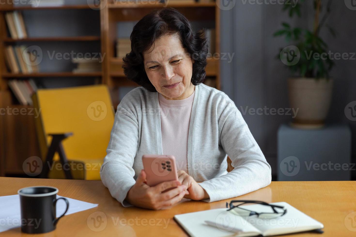 européen milieu vieilli Sénior femme en portant en utilisant téléphone intelligent toucher écran dactylographie faire défiler page. élégant plus âgée mature Années 60 Dame avec cellule téléphone en utilisant l'Internet social médias applications à maison. achats en ligne. photo