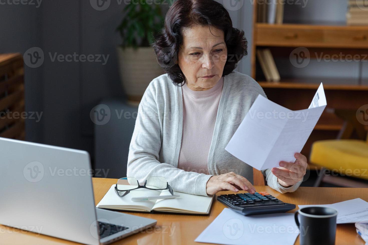 milieu vieilli Sénior femme asseoir avec portable et papier document, pensif plus âgée mature Dame en train de lire papier facture Payer en ligne à Accueil gérant banque finances calculateur les taxes Planification prêt dette Pension Paiement photo