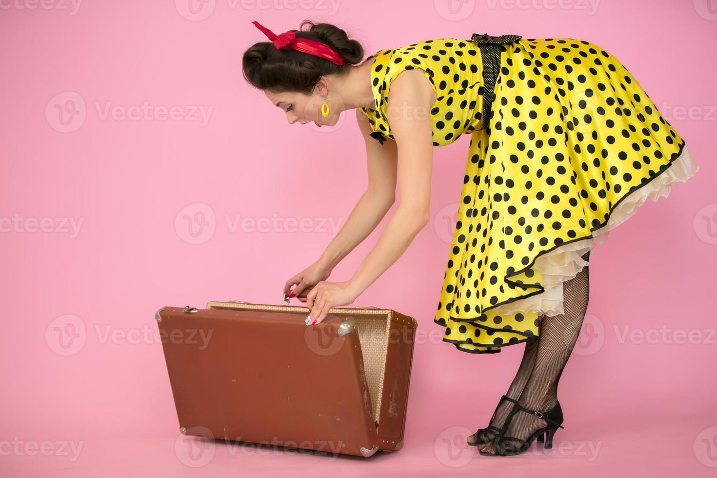 rétro fille ouvre un vieux valise sur une rose Contexte. photo