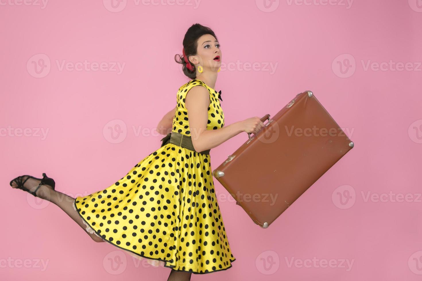 rétro fille avec un vieux valise sur une rose Contexte. photo