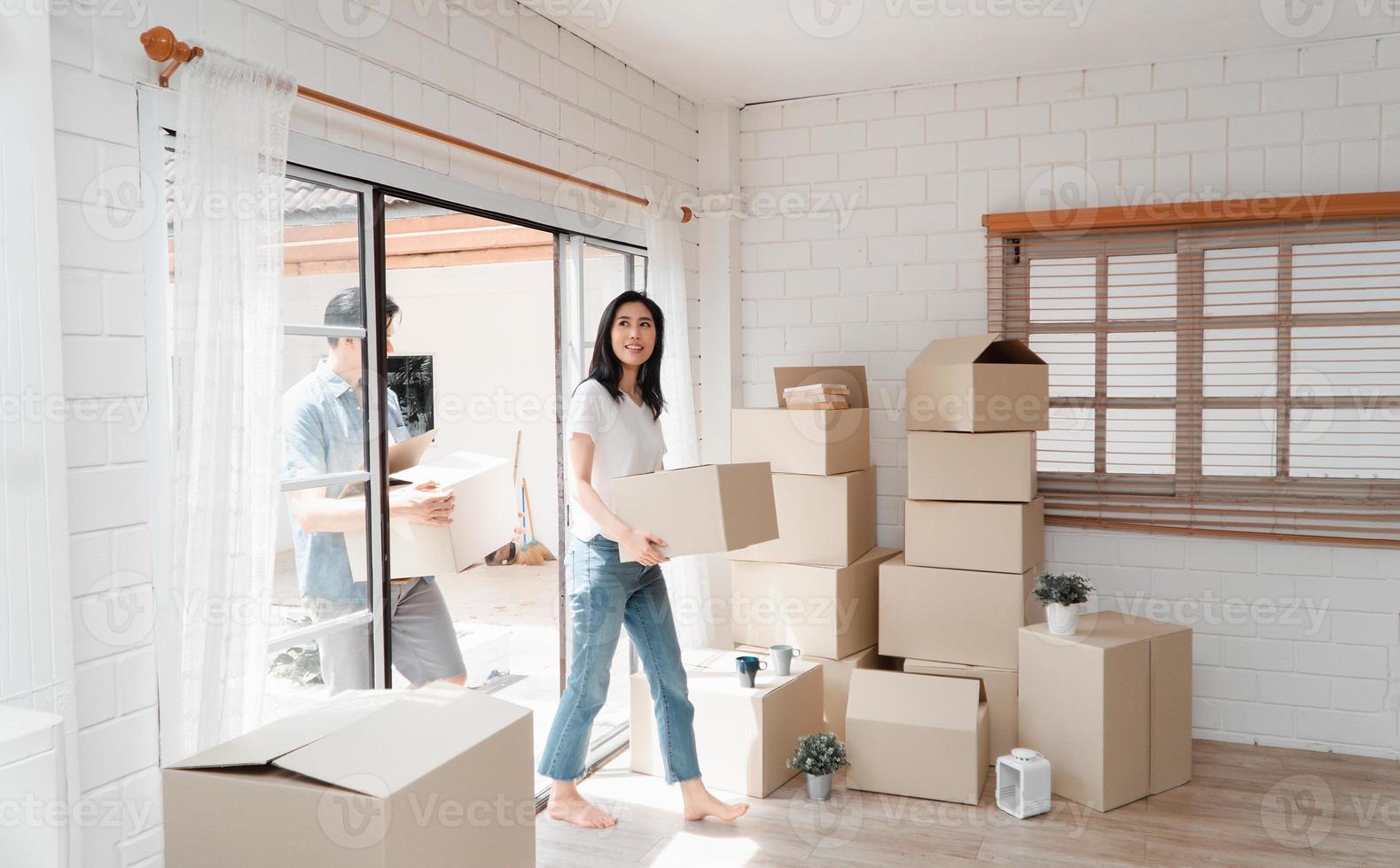 content Jeune couple porter papier carton des boites et en marchant de le de face porte dans le maison dans une Nouveau maison à en mouvement journée. concept de déménagement, de location, et propriétaire en mouvement à maison. photo