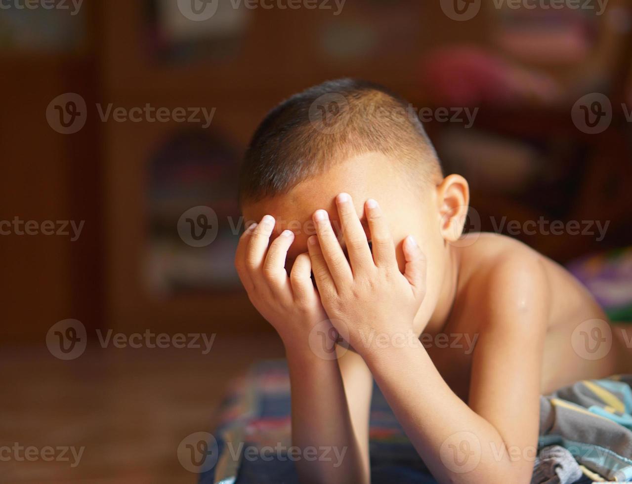 le garçon couvert le sien yeux avec le sien mains à bloquer le Soleil. photo