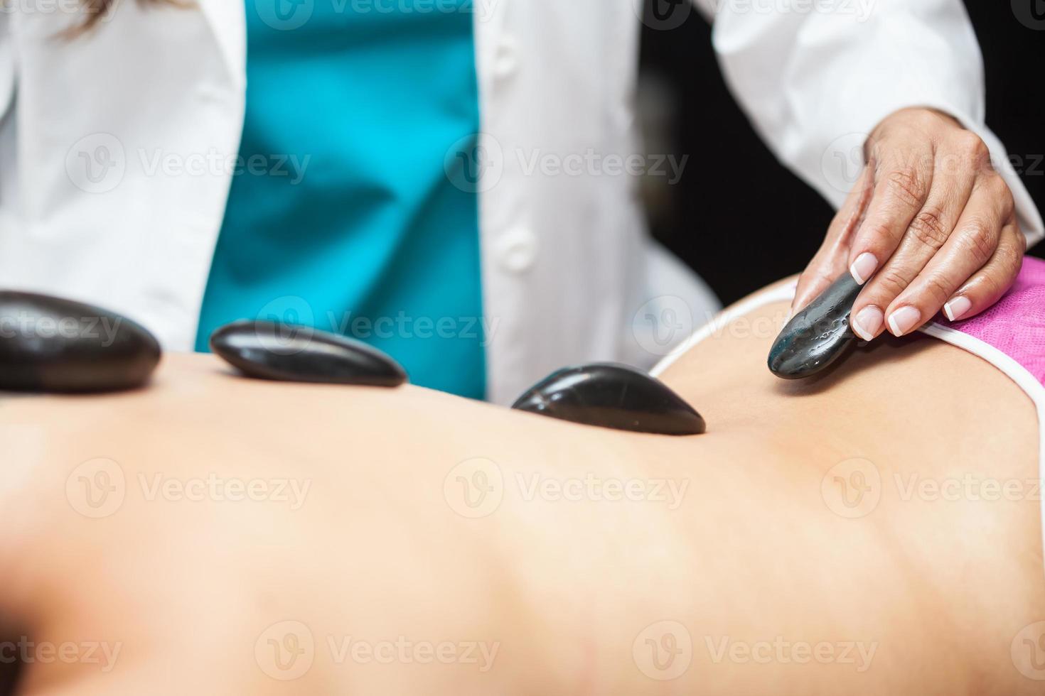 médecin performant une chaud volcanique des pierres thérapie sur une Jeune femelle patient retour photo