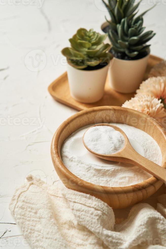 beauté concept de collagène poudre dans une en bois bol et cuillère sur blanc table Contexte. santé supplément, protéine admission. fleur et vert plante photo