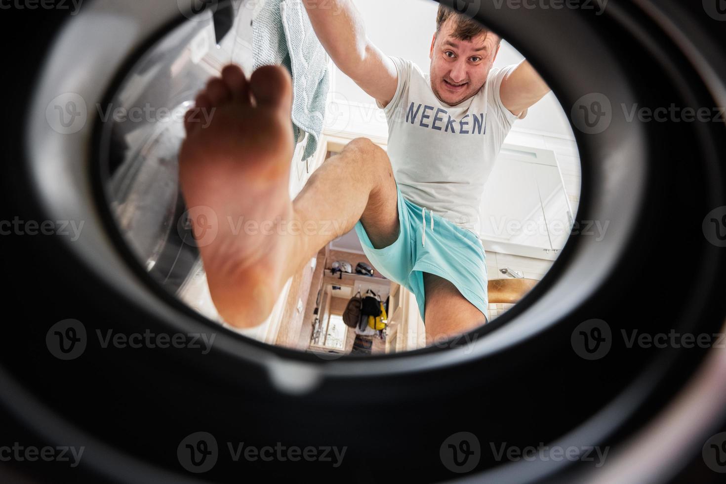 homme vue de la lessive machine à l'intérieur. Masculin Est-ce que du quotidien routine. grimpe à l'intérieur, pousser et pressage le blanchisserie avec le sien pieds. photo