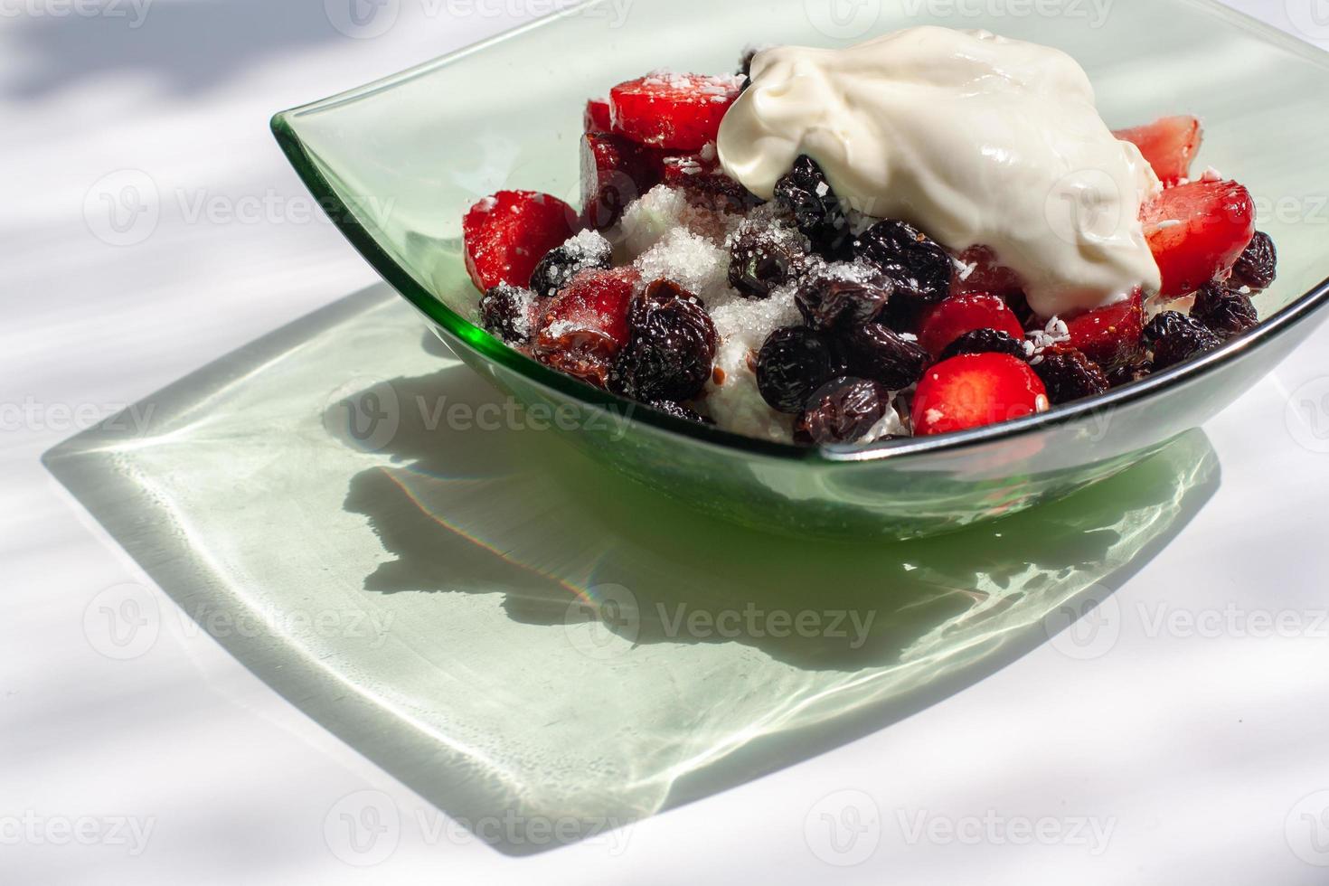 des fraises, raisins secs et chalet fromage avec acide crème dans une vert verre assiette sur une blanc Contexte. magnifique ombre de le plaque. en bonne santé petit déjeuner. horizontal. photo