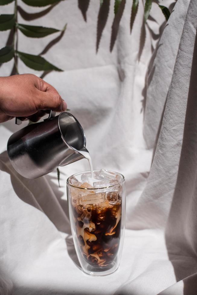 barista versant du lait dans un verre de café glacé photo