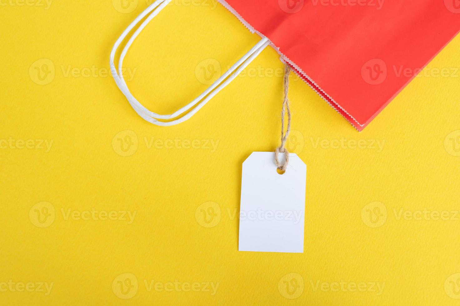 blanc étiquette avec une papier rouge sac pour recyclage sur une Jaune Contexte. papier sac poignées photo